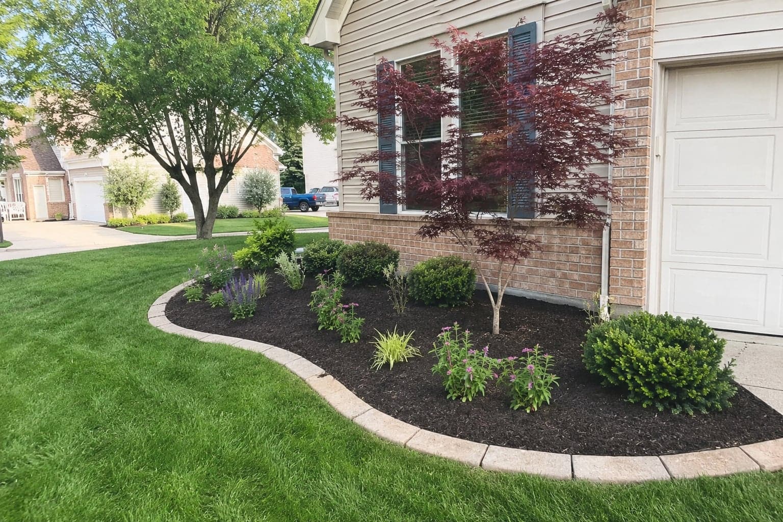 A newly installed landscape bed with shrubs and a stone border by First Class Property Services